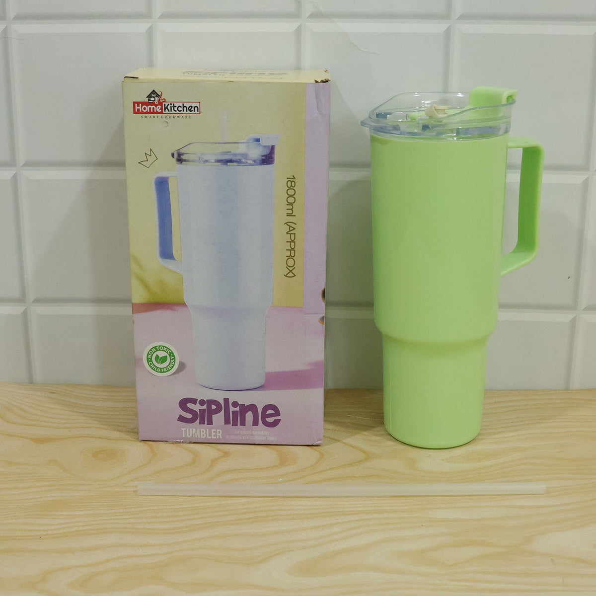 A light green travel tumbler with a handle, lid, and straw is displayed next to its product box on a wooden surface.