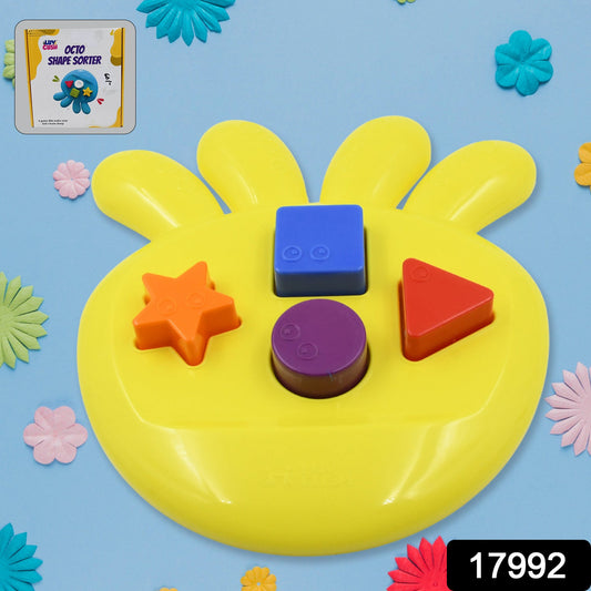 Yellow shape sorter with colorful blocks on a blue background surrounded by small decorative flowers and a product label.