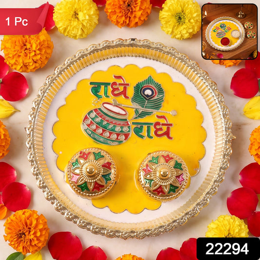 A silver and yellow Radhe Radhe pooja thali set with two small decorative containers, surrounded by marigolds and rose,