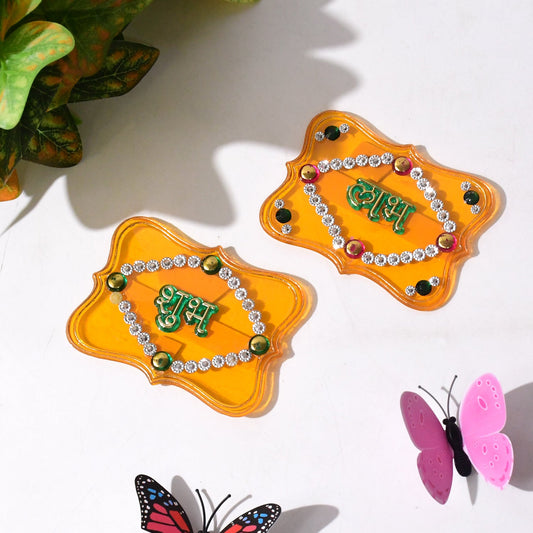 Two ornate yellow Shubh Labh wall hangings with green text and clear and colored jewels.