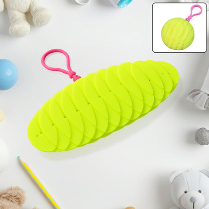 A bright green collapsible silicone ball keychain with a pink loop, shown partially collapsed on a white surface with toys,