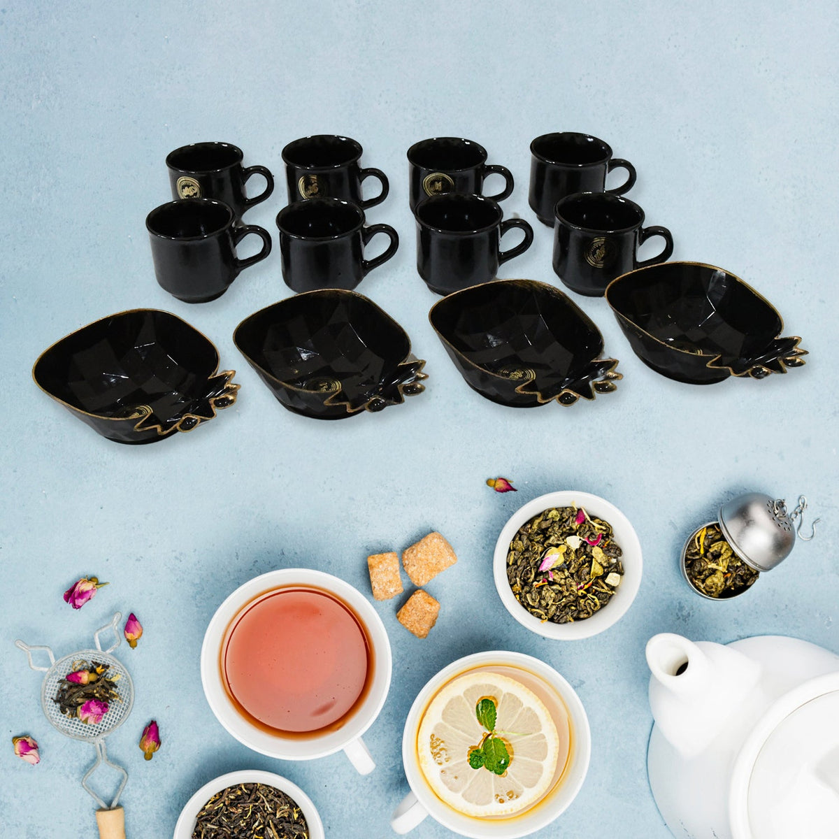 A black ceramic tea set with eight cups and four pineapple-shaped snack bowls on a blue surface, surrounded by tea leaves