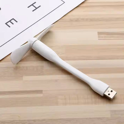 White USB fan with flexible neck lying on a light wooden surface next to a white paper.