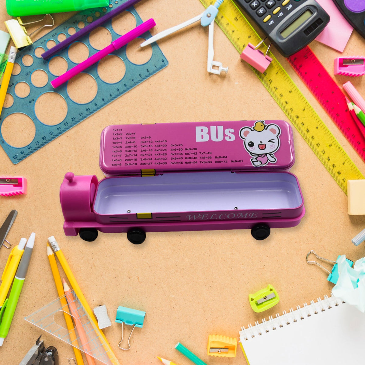 Open pink bus pencil case with a multiplication table on the lid, surrounded by school supplies on a wooden desk.