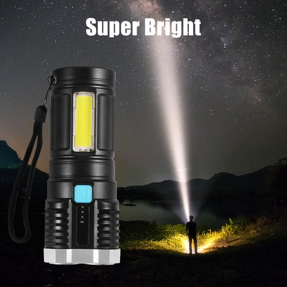 Black and silver flashlight with a wrist strap, illuminating a person standing in a dark landscape under a starry night sky.