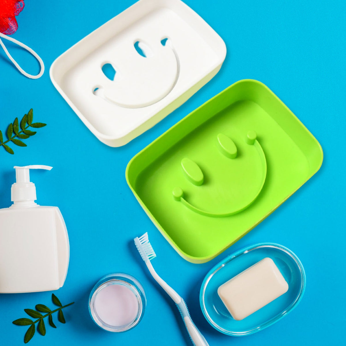 A green and a white soap dish, both with smiley face designs, surrounded by bathroom items on a blue background.