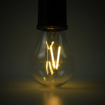 A close-up of the clear LED bulb shows its warm yellow filaments glowing brightly against a dark background.