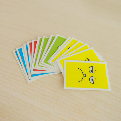 A fan of colorful cards, each depicting a different facial expression, is spread out on a light wooden surface.