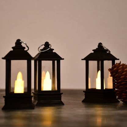 Three black lanterns with bright LED candles and a pinecone on a dark surface, creating a warm ambiance.