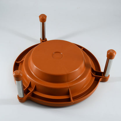 Underside view of the orange plastic stand with three silver legs and brown caps, on a white surface.