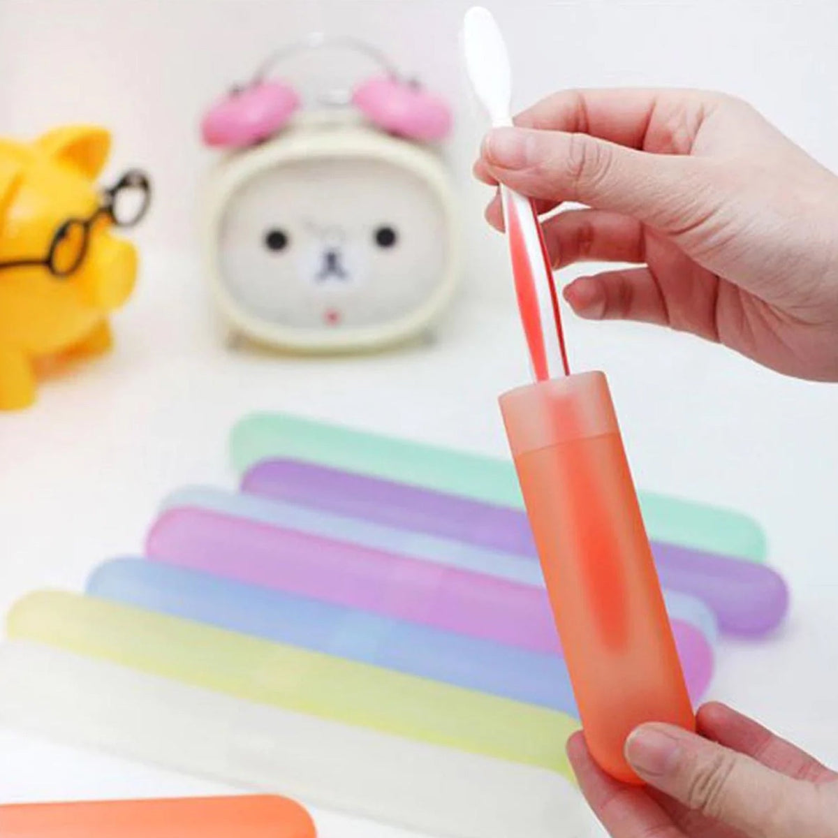 A hand inserts a white toothbrush into a translucent orange case, with other pastel-colored cases in the background.