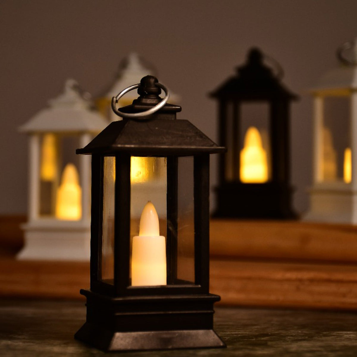 A close-up of a black lantern with a flickering LED candle, surrounded by other blurred lanterns in the background.