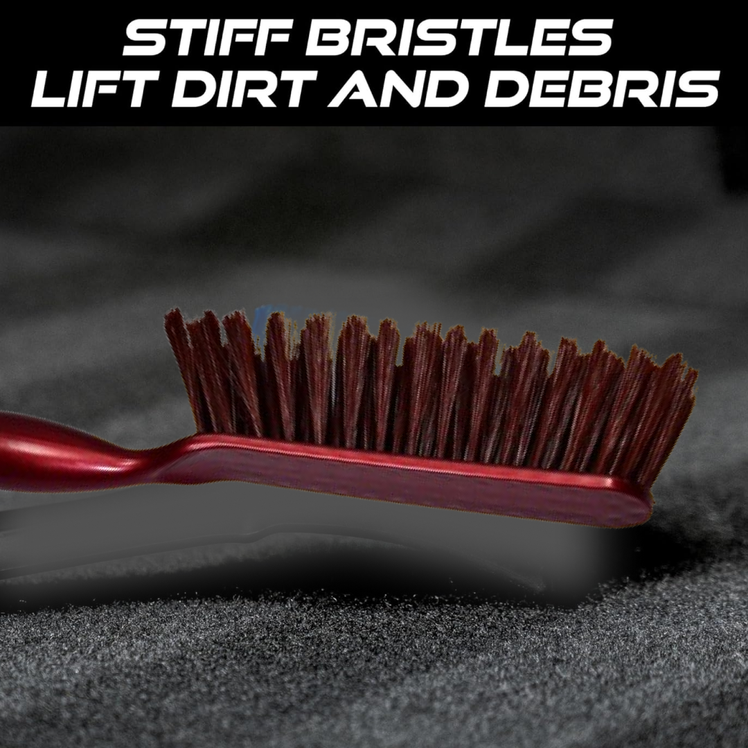 A close-up of the red and white handled brush with brown bristles on a dark textured surface, with text about stiff bristles.