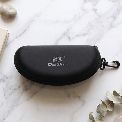 Closed black hard shell sunglasses case with a white logo and clip, resting on a white marble surface with foliage.
