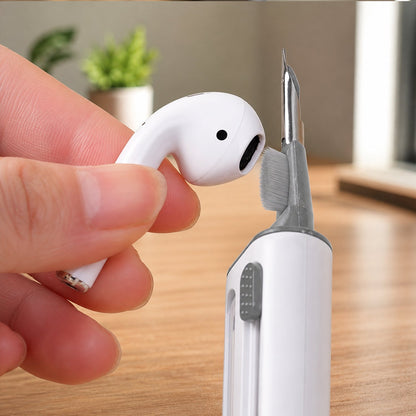 A hand holding a white earbud while the cleaning pen's small brush cleans the earbud speaker.