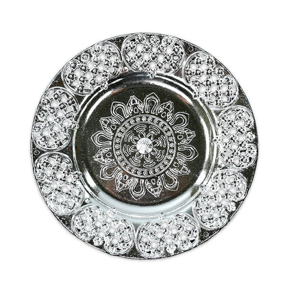 A top-down view of a round, silver-colored plastic pooja thali with intricate embossed patterns and a filigree edge.