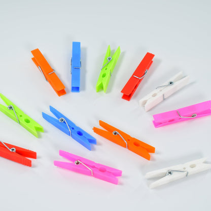 Twelve colorful plastic clothes clips scattered on a white surface, showing various colors and their metal springs.