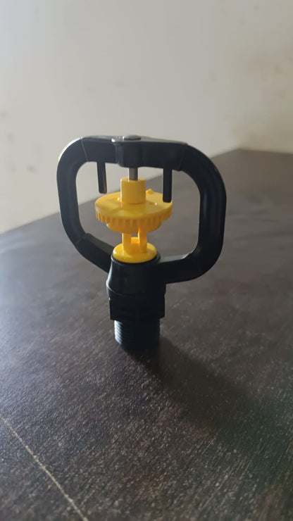 A black and yellow rotating sprinkler nozzle resting on a dark brown surface.