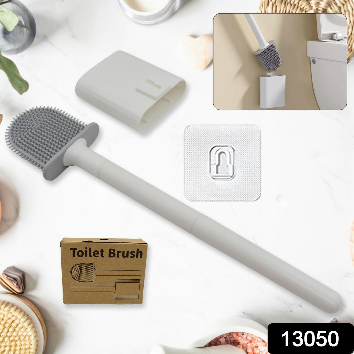 A gray silicone toilet brush, wall holder, adhesive hook, and a small brown box are displayed on a white surface.