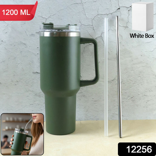 A dark green insulated travel mug with a handle, clear lid, and two straws (one clear, one metal) stands against a grey wall.