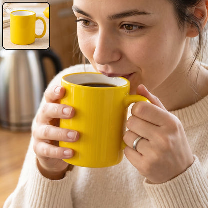 A woman in a cream sweater sips from a bright yellow mug with a white interior, holding it with both hands.