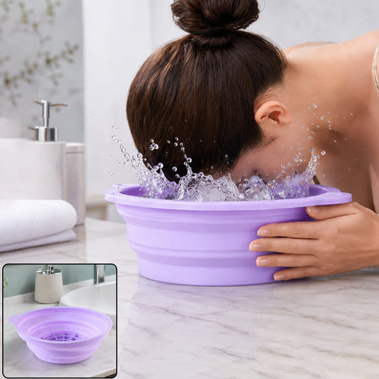 A woman splashes her face in a purple collapsible silicone bowl filled with water and ice cubes on a marble counter.