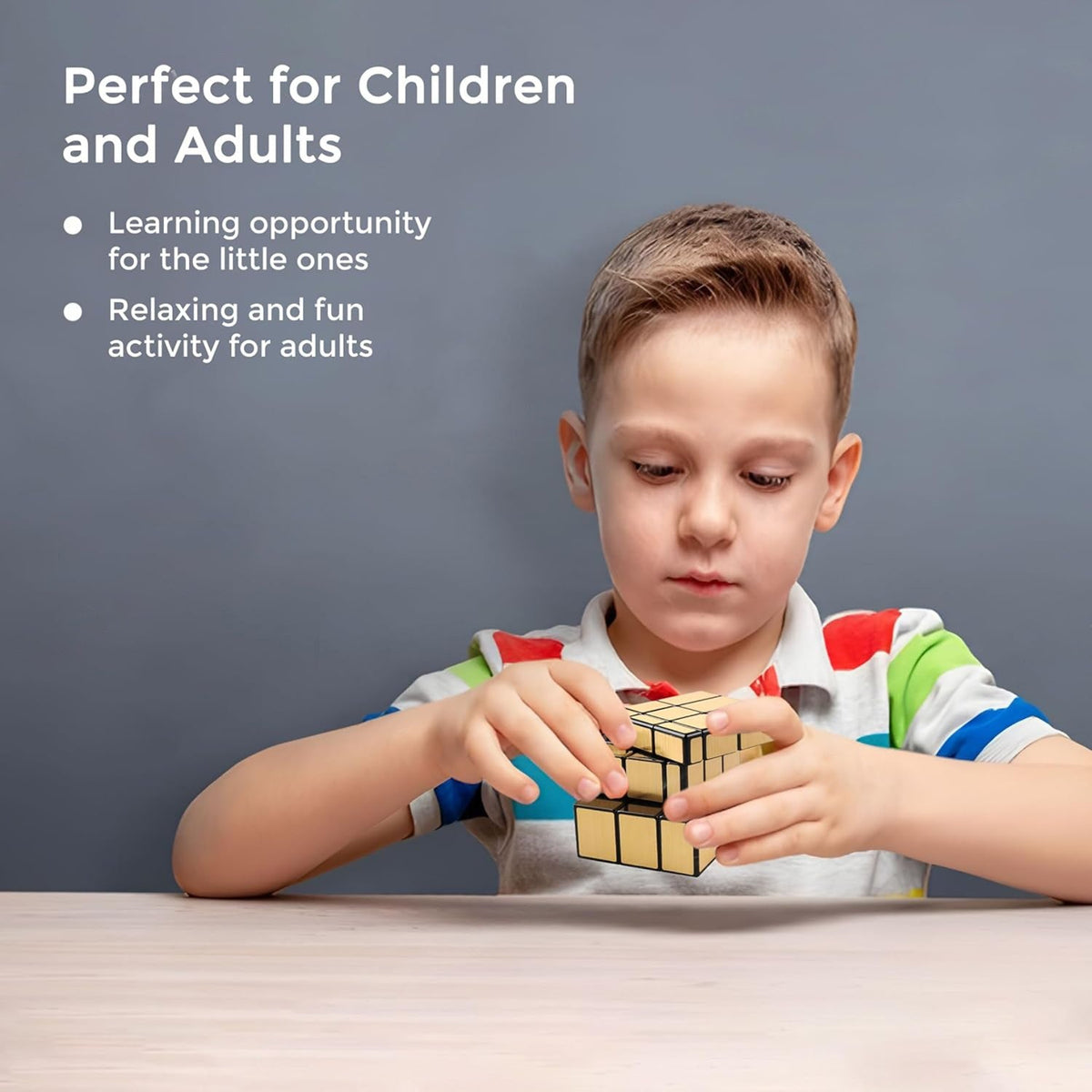 A young boy with a striped shirt is focused on solving a gold mirror cube puzzle at a light wooden table.
