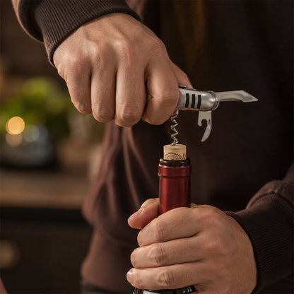 A hand uses the silver multi-tool's screwdriver to tighten a bolt on a bicycle fender.