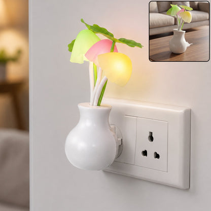 A white vase-shaped night light with glowing pink, yellow, and green mushroom-like lights plugged into a wall outlet. A