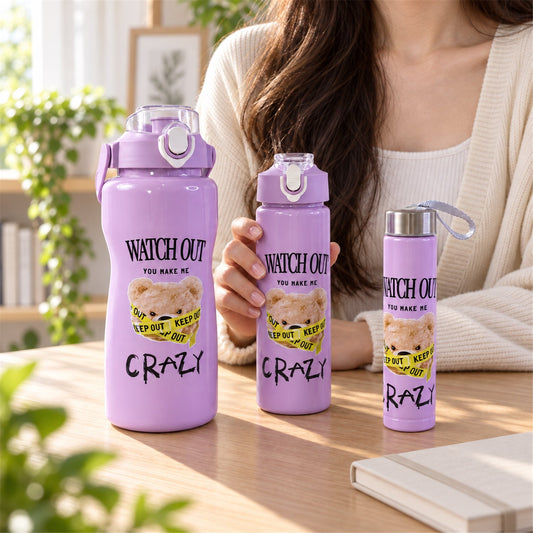 Three purple water bottles with a teddy bear design, in varying sizes, on a wooden table with a person in the background.