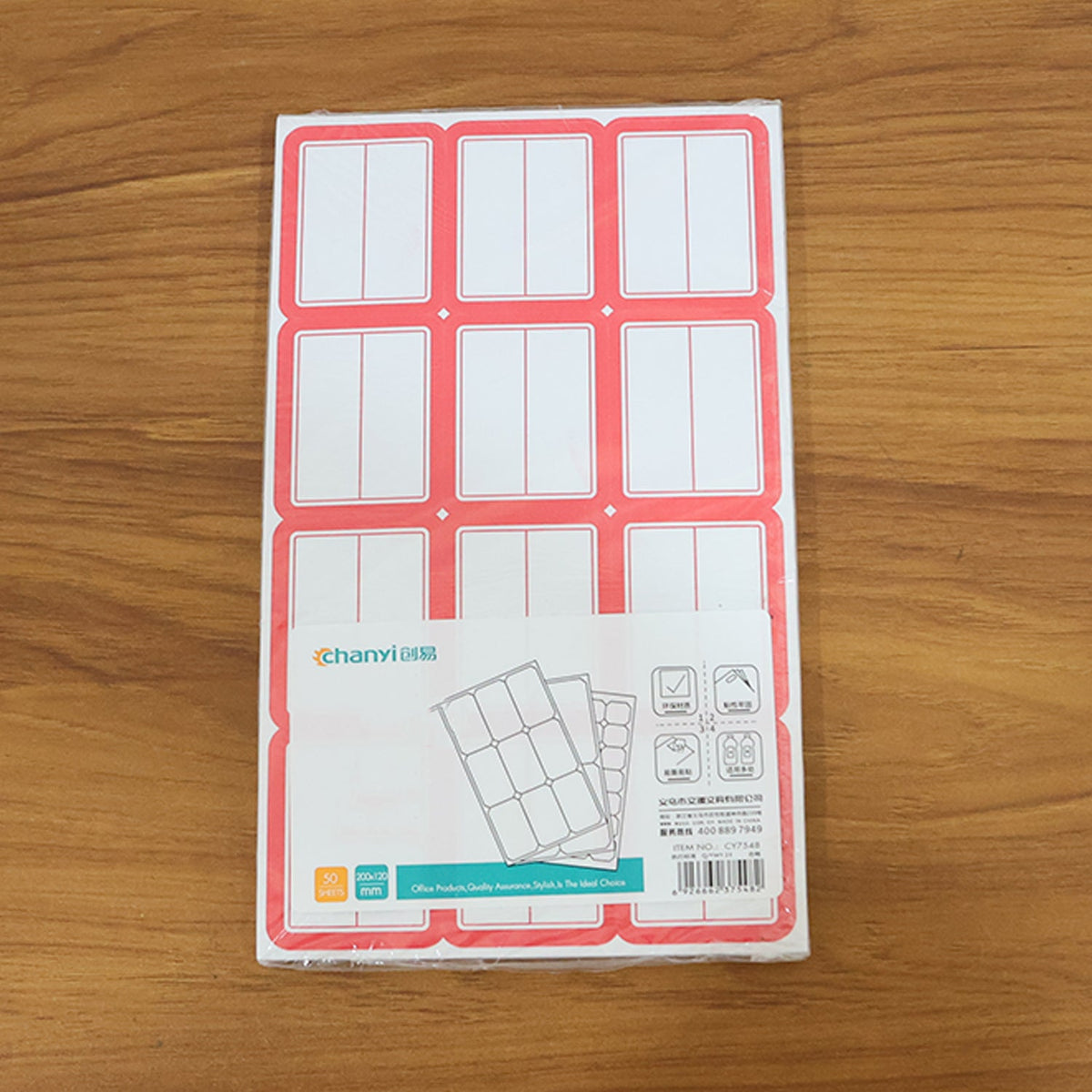 A packaged stack of red-bordered white writable label sheets with product information on a wooden surface.
