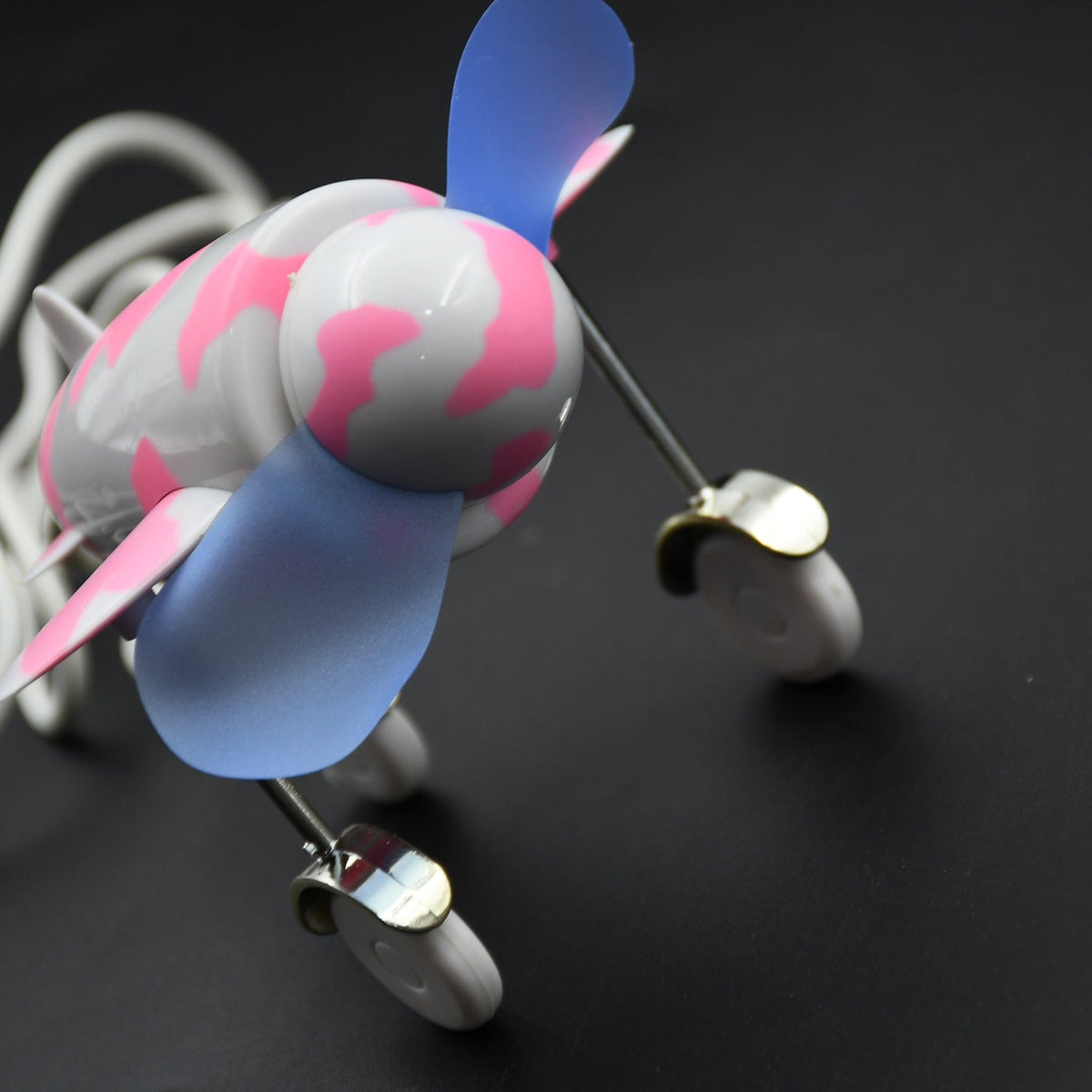 A low-angle view of the pink and white airplane USB fan, highlighting its blue propellers and attached wheels.