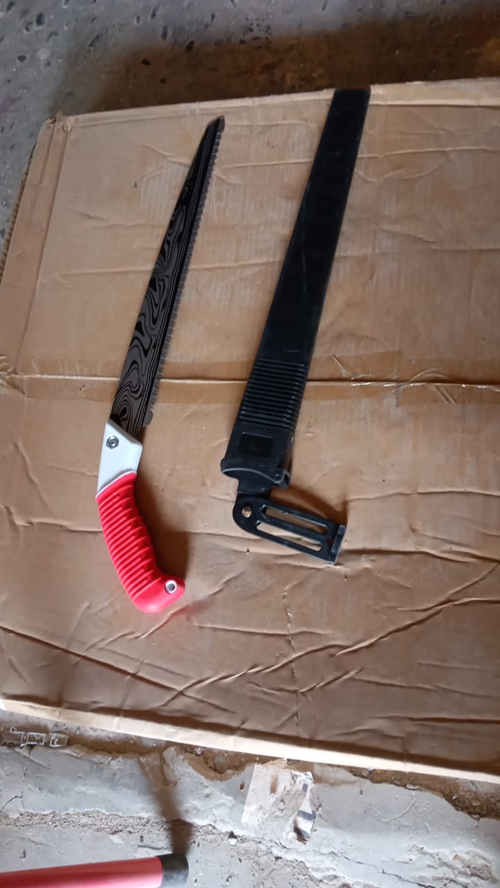 A hand pruning saw with a red handle and its black sheath resting on a cardboard box with a textured surface.