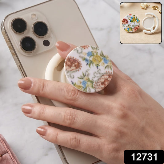 A hand holds a white smartphone with a round pop socket featuring a white background and colorful paisley floral pattern.