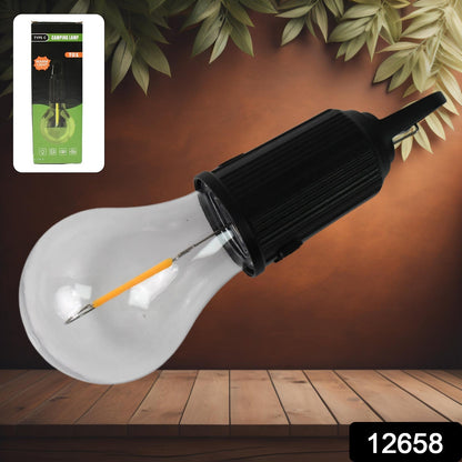 A clear LED bulb with a black top and hook lies on a wooden surface, with its green and black packaging in the top left.