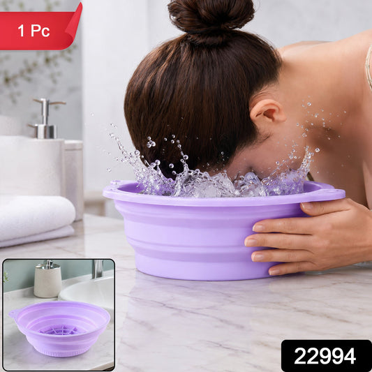A woman splashes her face in a purple collapsible silicone bowl filled with water and ice cubes on a marble counter. – view 2
